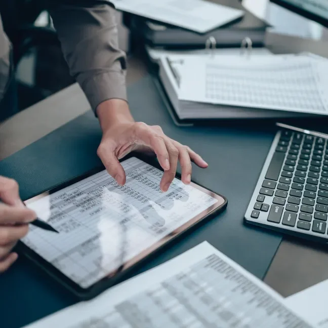 Finance spreadsheet on a tablet screen with computer keyboard and paperwork nearby